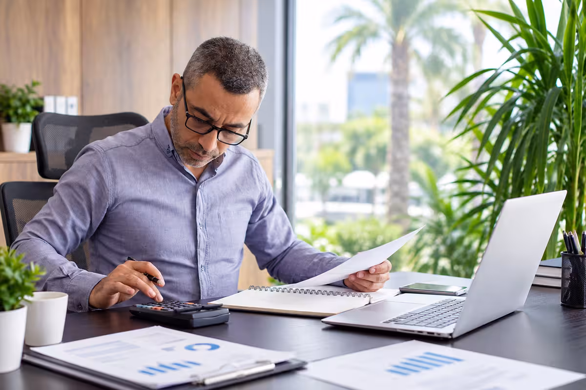 Professional reviewing financial paperwork with a calculator and laptop