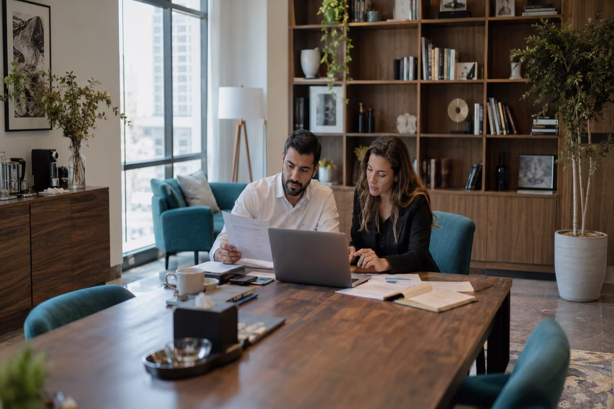 Business owner and accountant reviewing ledger records and a laptop in a spacious office